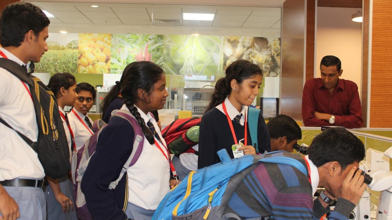 A group of students in uniforms observe and use lab equipment while accompanied by an adult in a science facility.