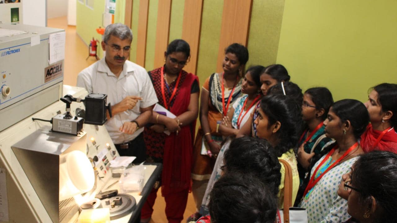 A man demonstrates a machine to a group of students in a classroom setting.