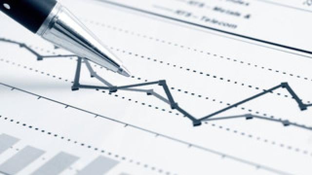 A pen points to a line graph on a sheet of paper with data columns and bar charts, indicating fluctuating trends.