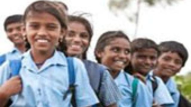 A group of children in school uniforms stand outdoors, smiling.