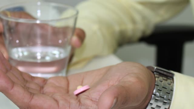 A person holding a glass of water in one hand and pills in the other.