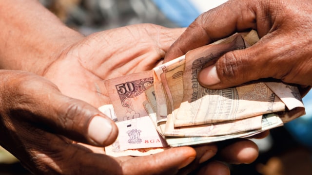 Two hands exchanging currency notes.