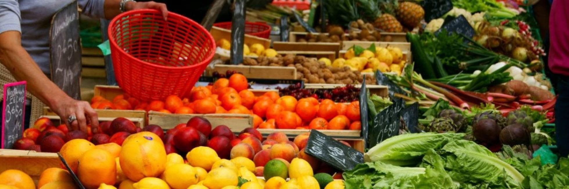 A variety of fruits and vegetables on display at a market, including oranges, peaches, lettuce, and more, with shoppers selecting produce.