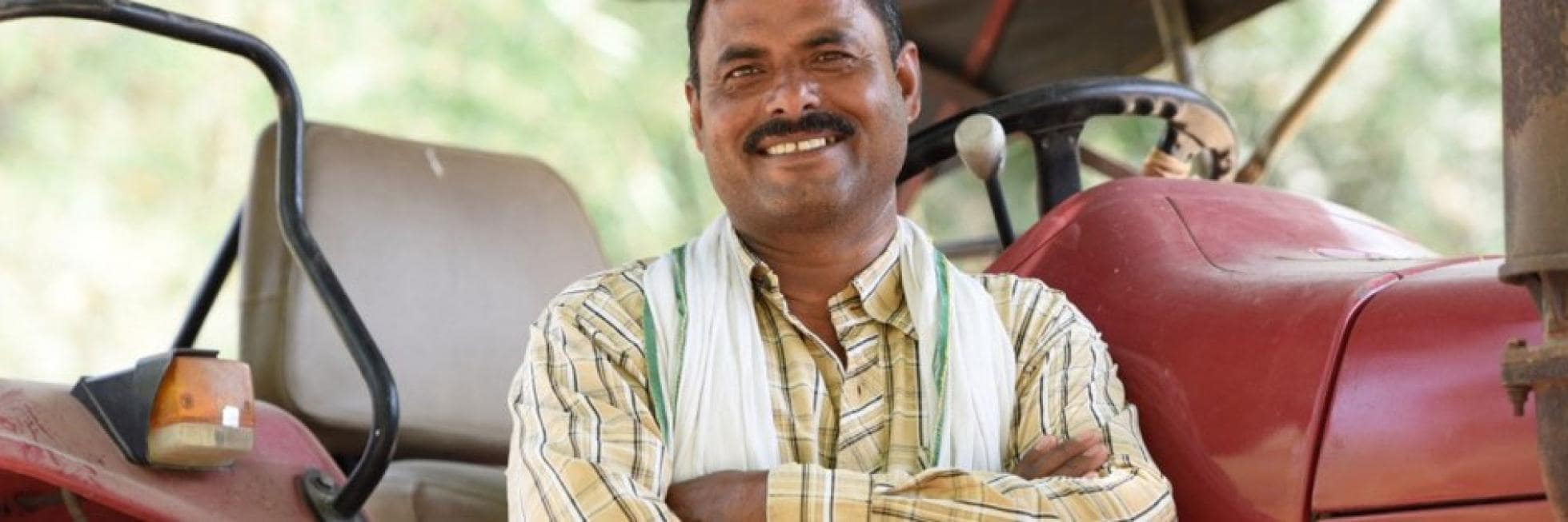 Man in a striped shirt smiling with arms crossed, standing next to a red tractor.
