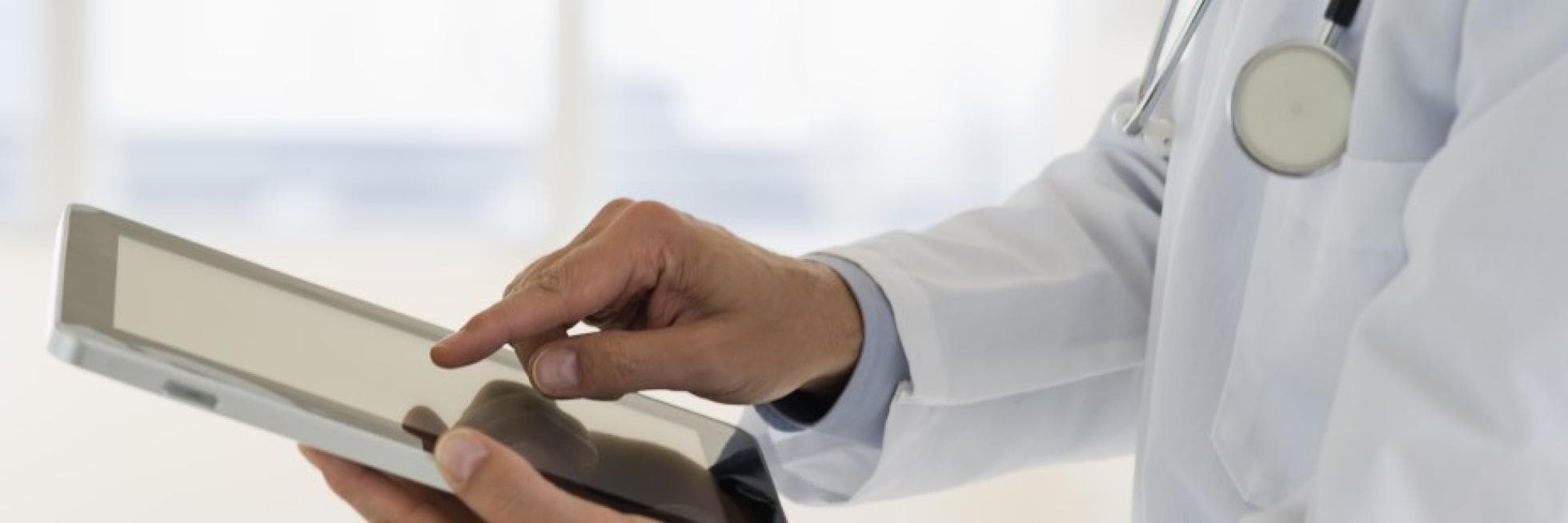 A doctor in a white coat uses a tablet.