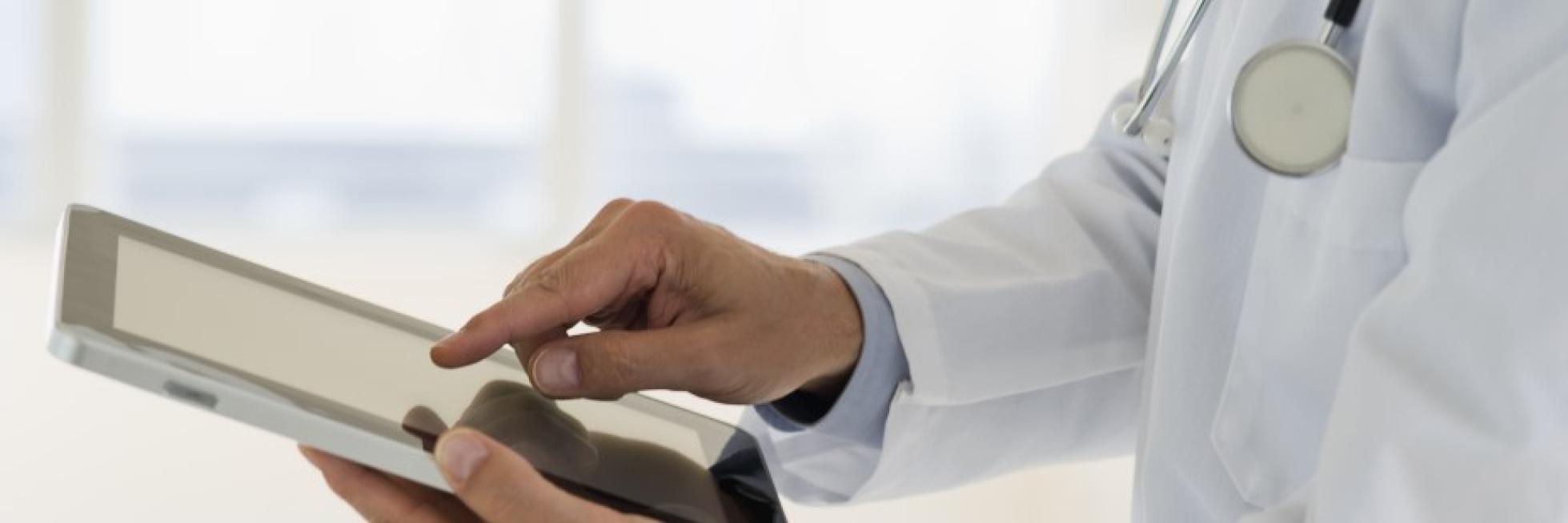 A doctor in a white coat uses a tablet.
