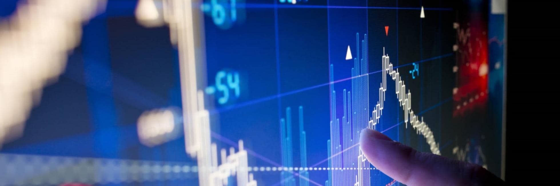 Fingers pointing at a digital screen displaying fluctuating financial graphs and numbers. Several data points and lines illustrate stock market trends.