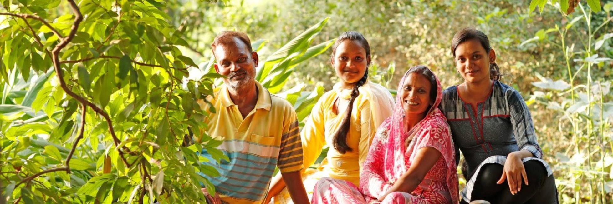 A family of four sits outdoors amid lush greenery.