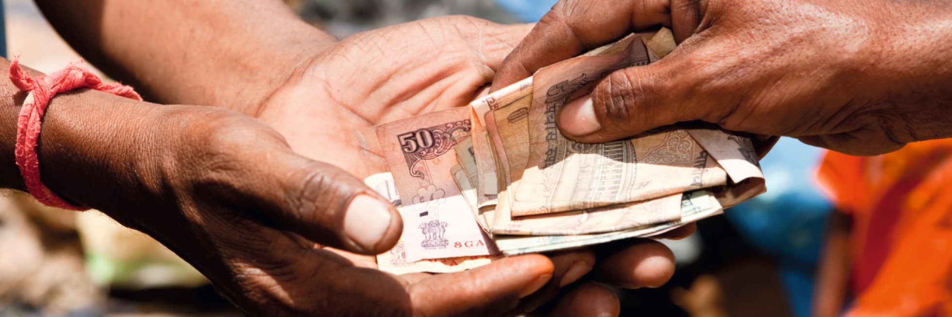 Two hands are exchanging a stack of Indian rupee banknotes, including a visible 50-rupee note.