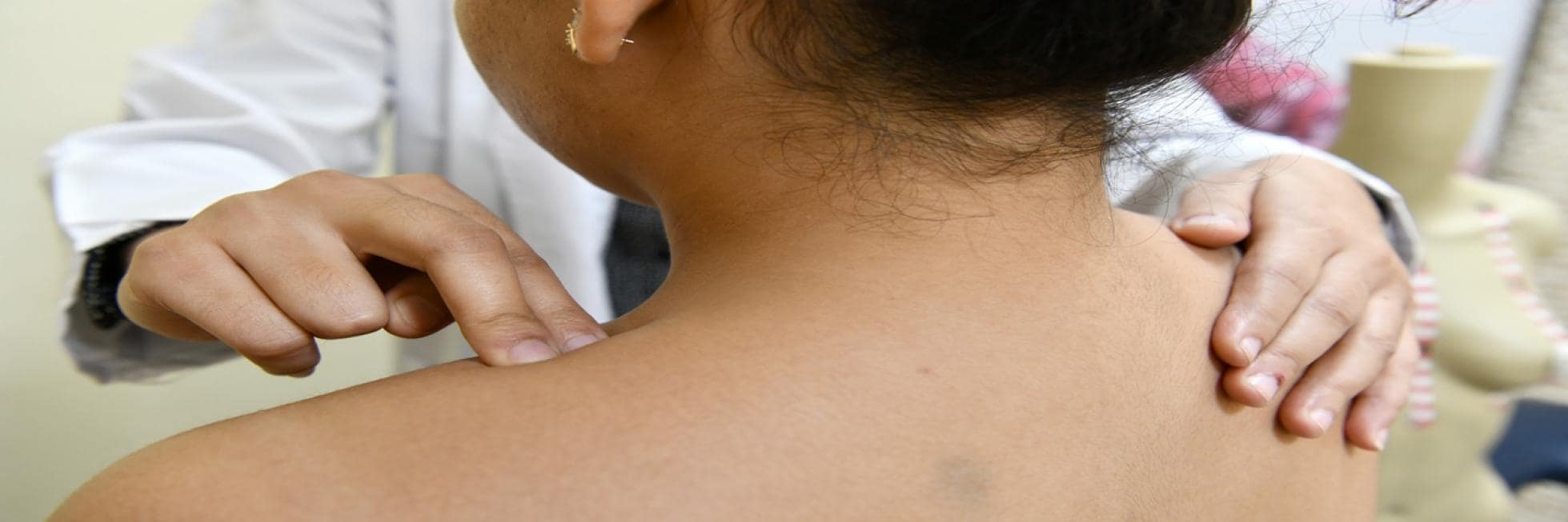 A person is examined by a healthcare professional who is pressing on their upper back.