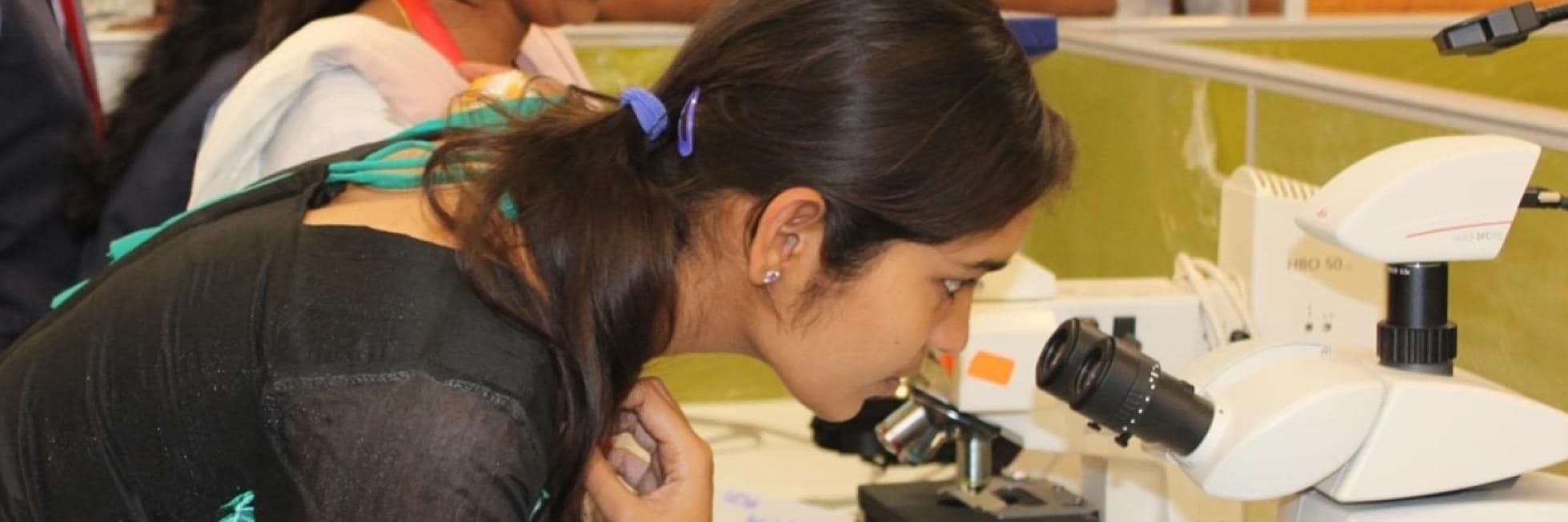 A woman looks intently through a microscope, surrounded by other scientific equipment.