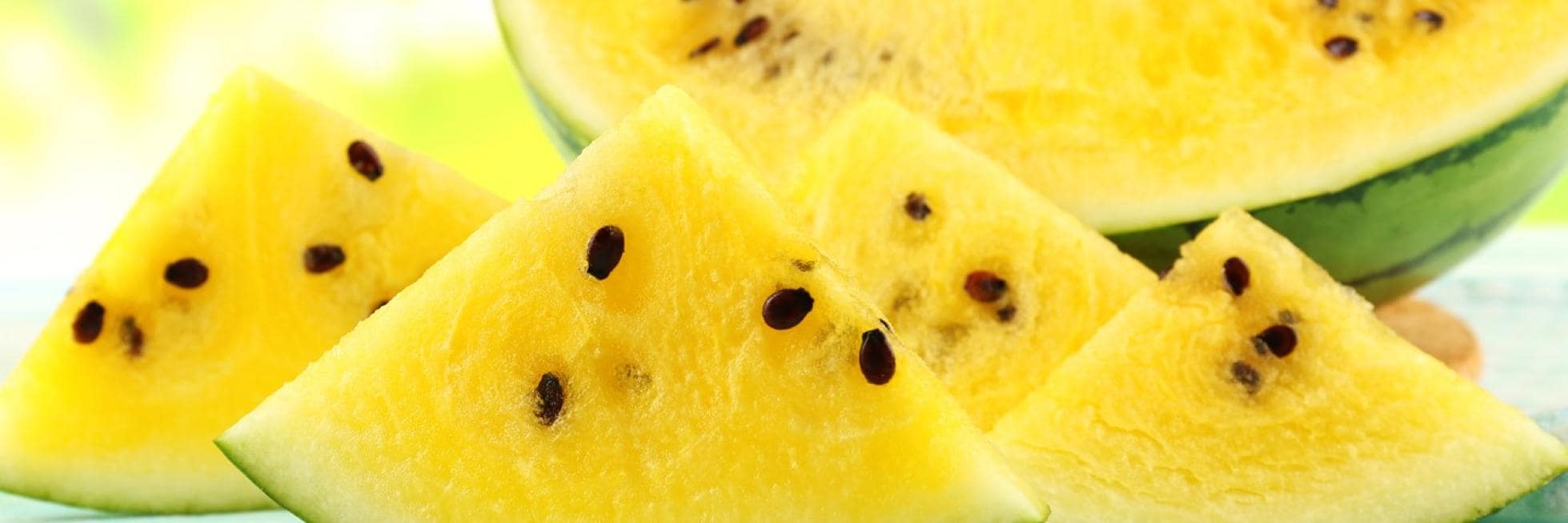 Slices of yellow watermelon with seeds, displayed on a light blue surface.