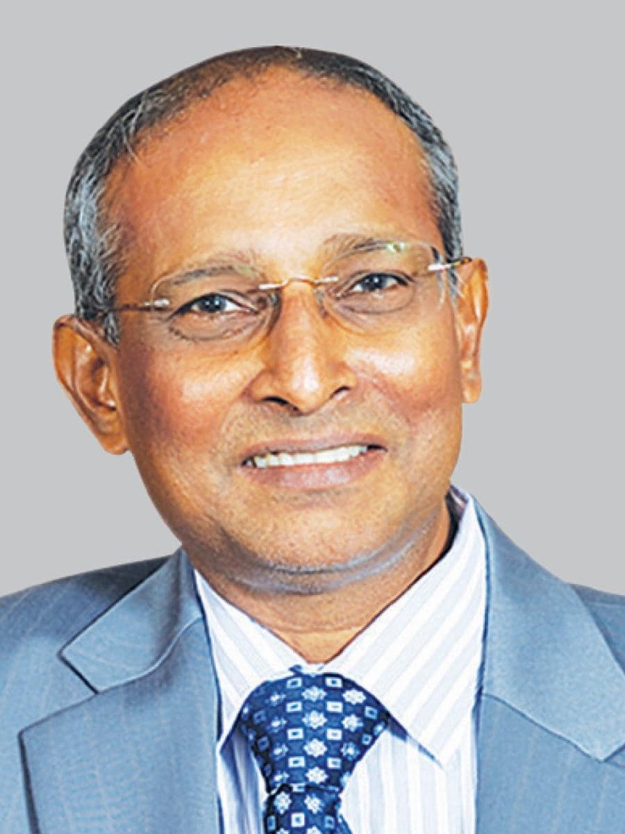 A man in a suit and tie smiles against a plain gray background.