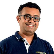 Smiling person wearing glasses and a dark polo shirt with logo, standing against a plain white background.