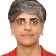 Person with short gray and black hair, wearing a red top, hoop earrings, and a nose ring, against a plain white background.
