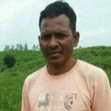 A person standing outdoors on a grassy field, wearing a light pink shirt.